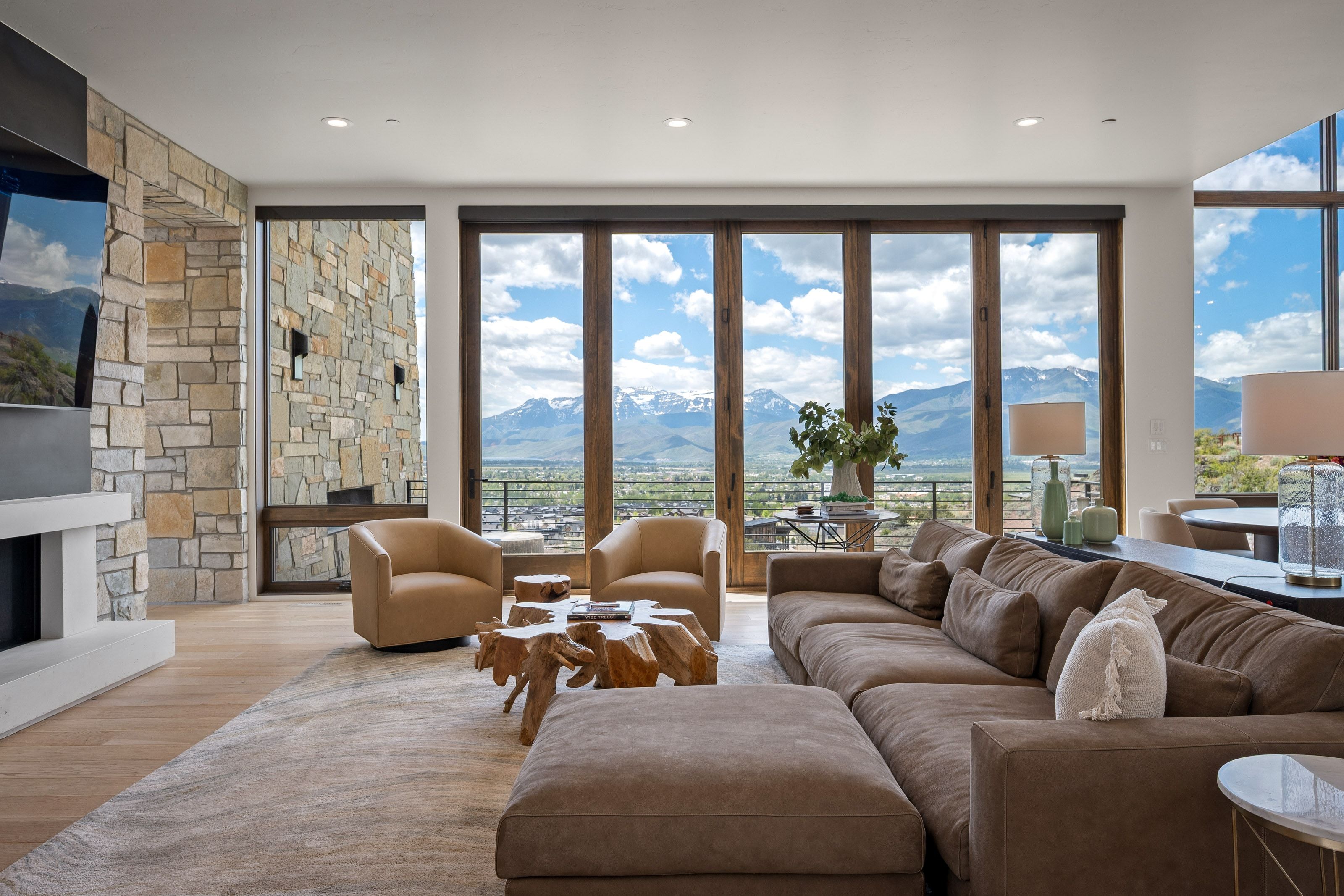 Expansive living space featuring a floor-to-ceiling stone fireplace, wood-finish flooring, and large bi-fold glass doors