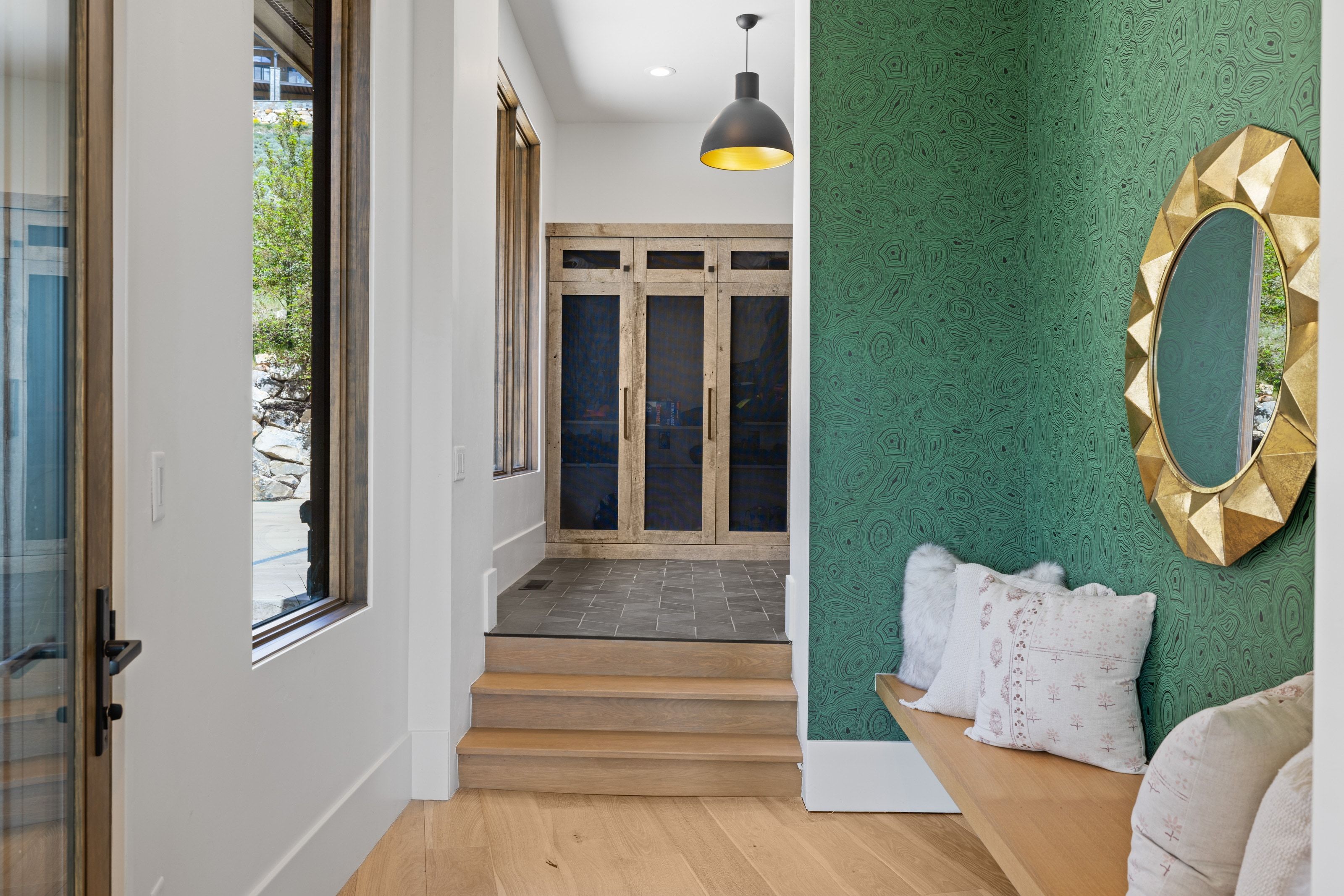 Foyer featuring wood-finish flooring, a wall with patterned green wallcovering, a built-in wood bench, and a gold-framed mirror