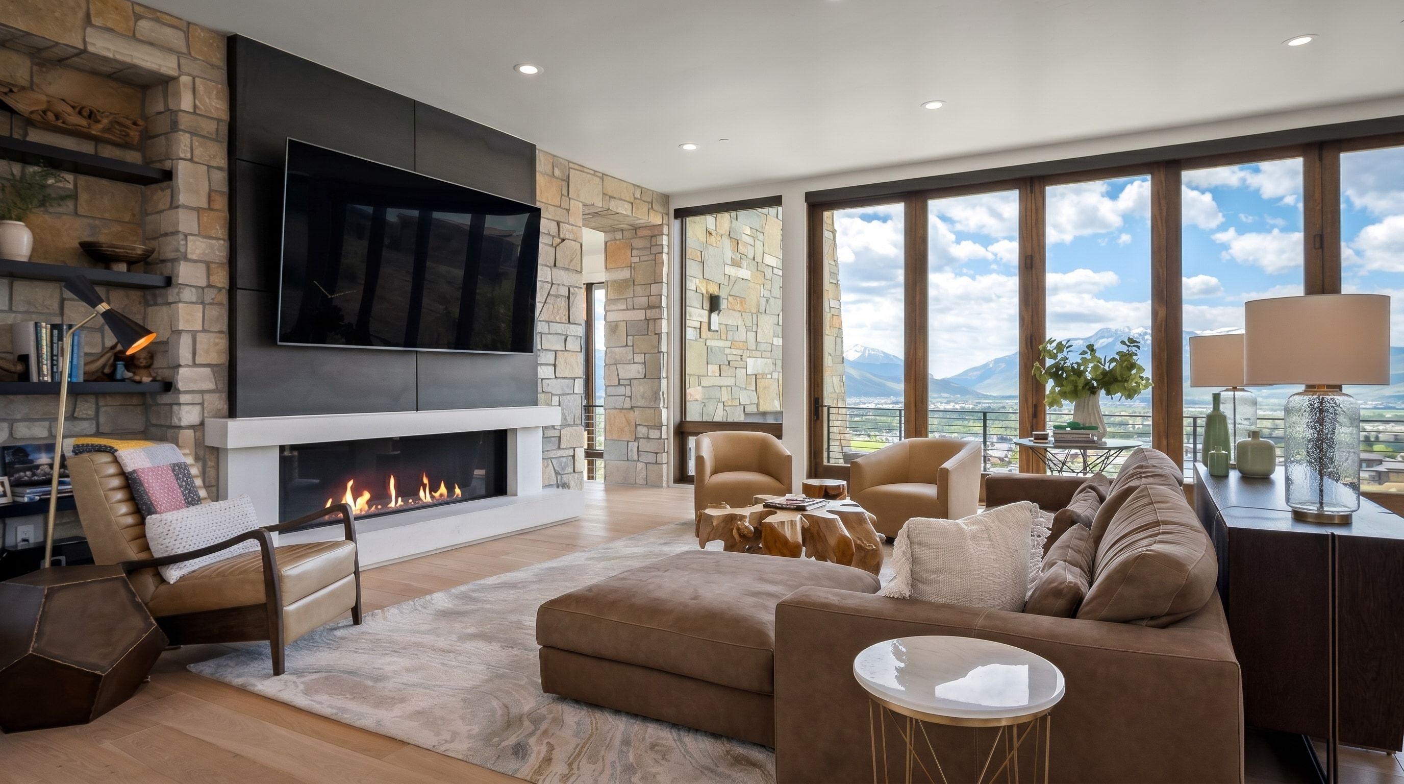 Spacious living area featuring a stone accent wall with built-in shelving, a linear fireplace with a white mantel, an integrated television mount, light wood-finish flooring, and large picture windows