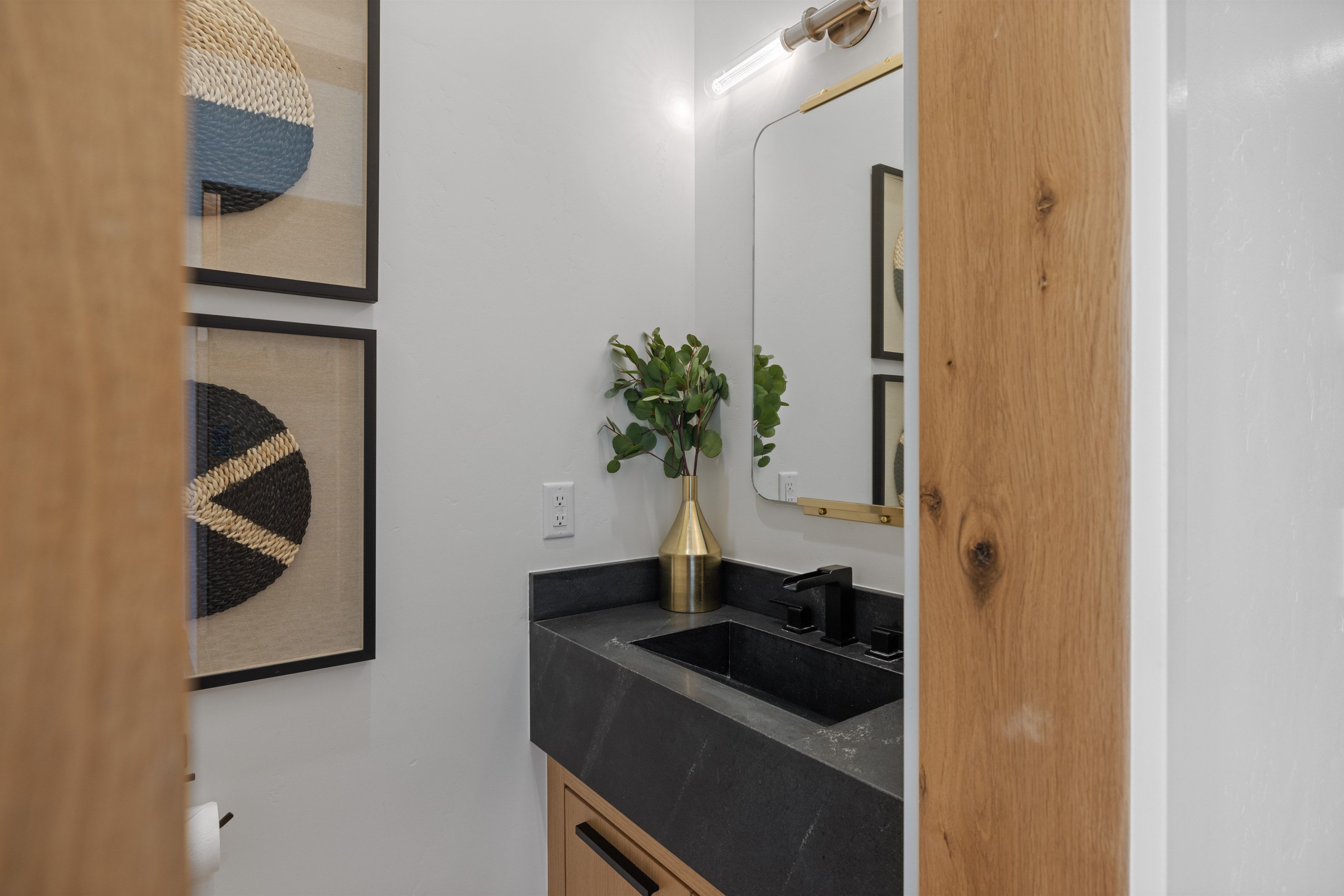 Vanity featuring a dark countertop with an integrated sink, matte black faucet, and brass-framed mirror