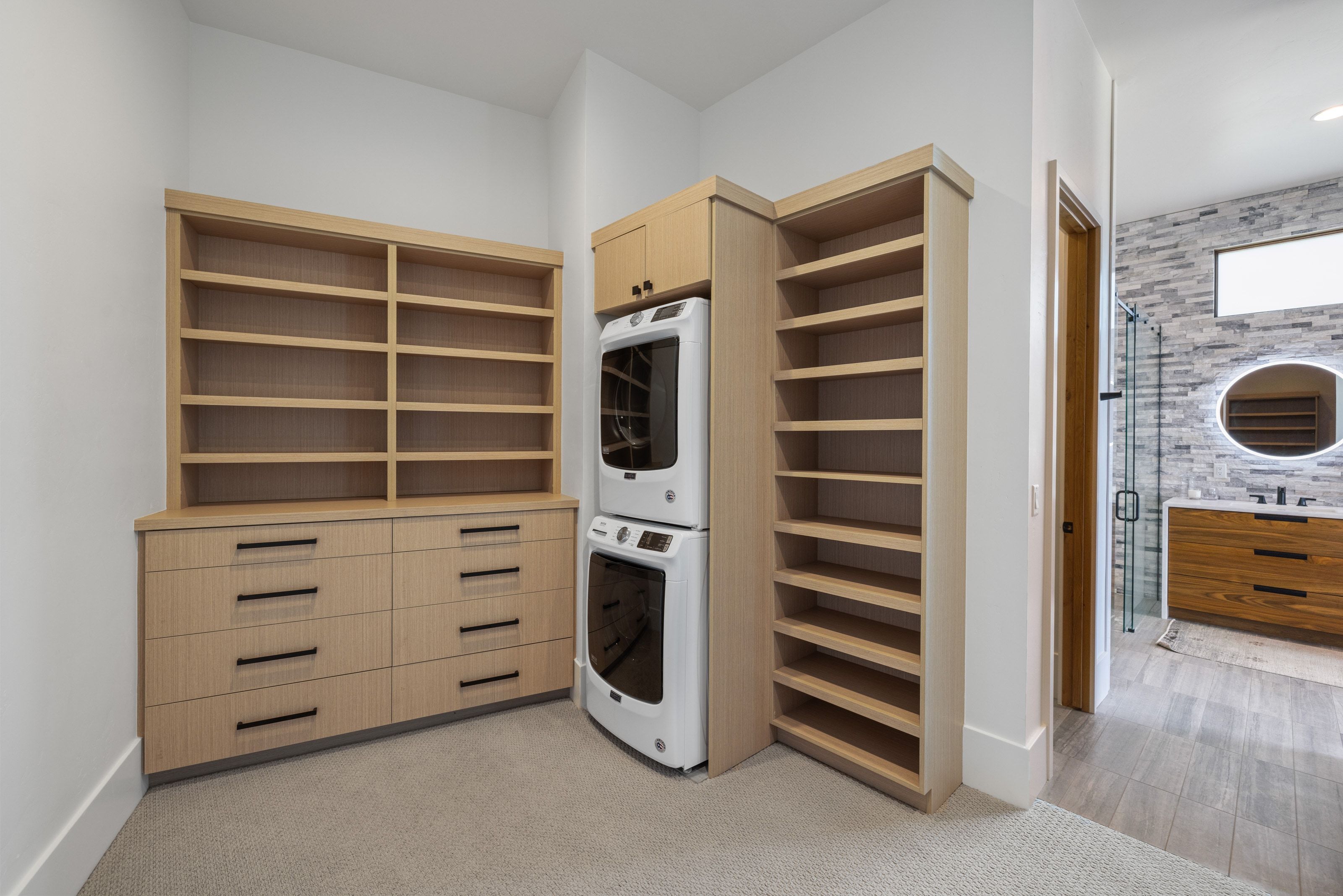 Custom built-in cabinetry with extensive shelving and storage drawers, wood-finish flooring, and a stackable washer and dryer unit