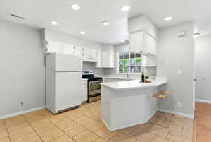 Kitchen featuring white cabinetry, stainless steel range, ceramic tile flooring, recessed lighting, and a breakfast bar