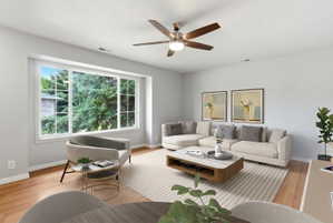 Spacious living area featuring a large picture window, wood-finish flooring, a ceiling fan with integrated lighting, and neutral wall tones