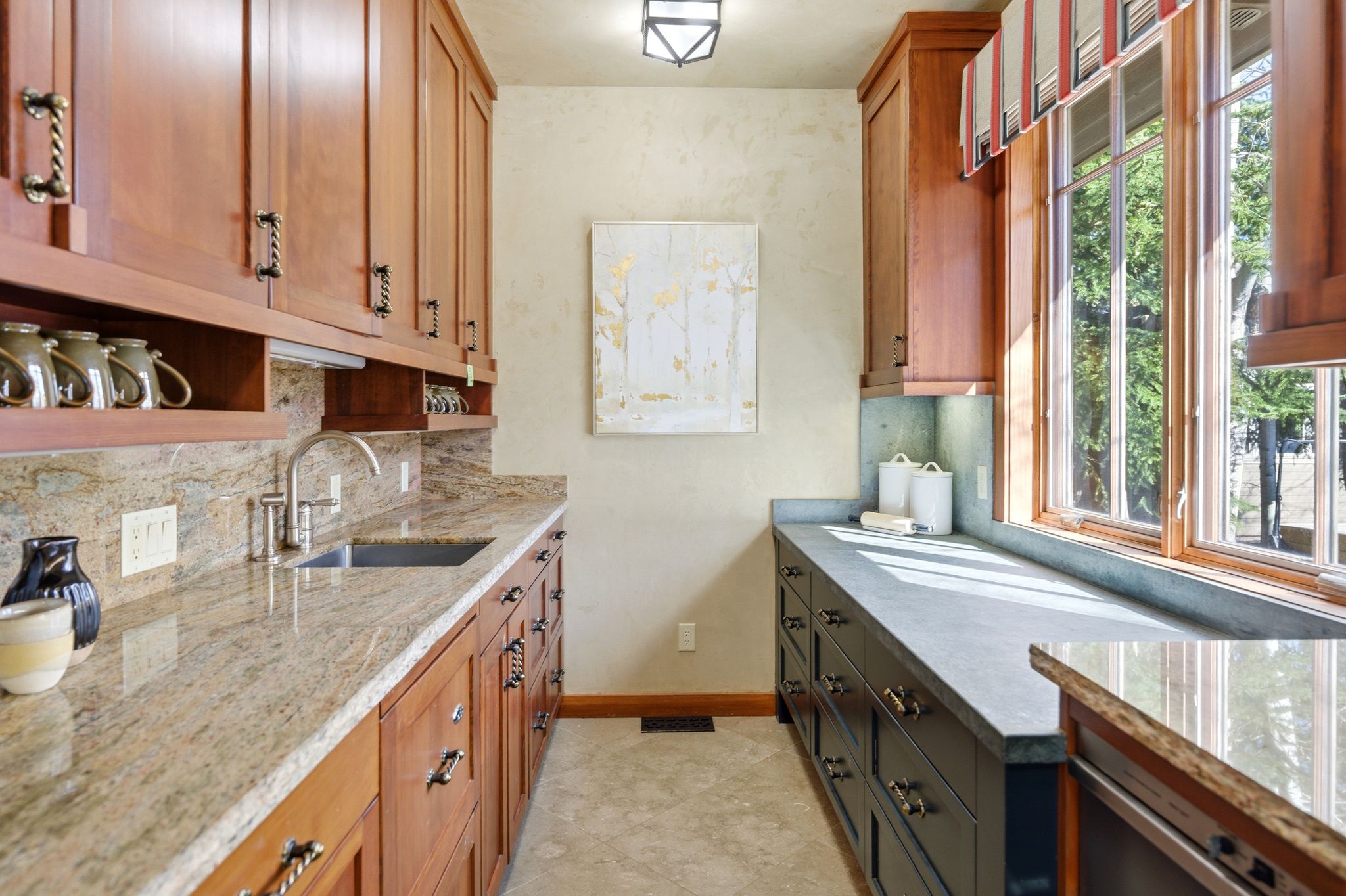 Galley-style service area featuring a stainless steel sink with a gooseneck faucet, light-toned granite countertops with a matching backsplash, and custom wood cabinetry
