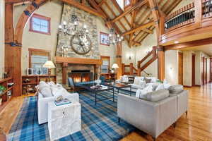 Spacious living area featuring a vaulted wood-beam ceiling, stone-clad fireplace with a wood mantle, wood-finish flooring, and a built-in staircase