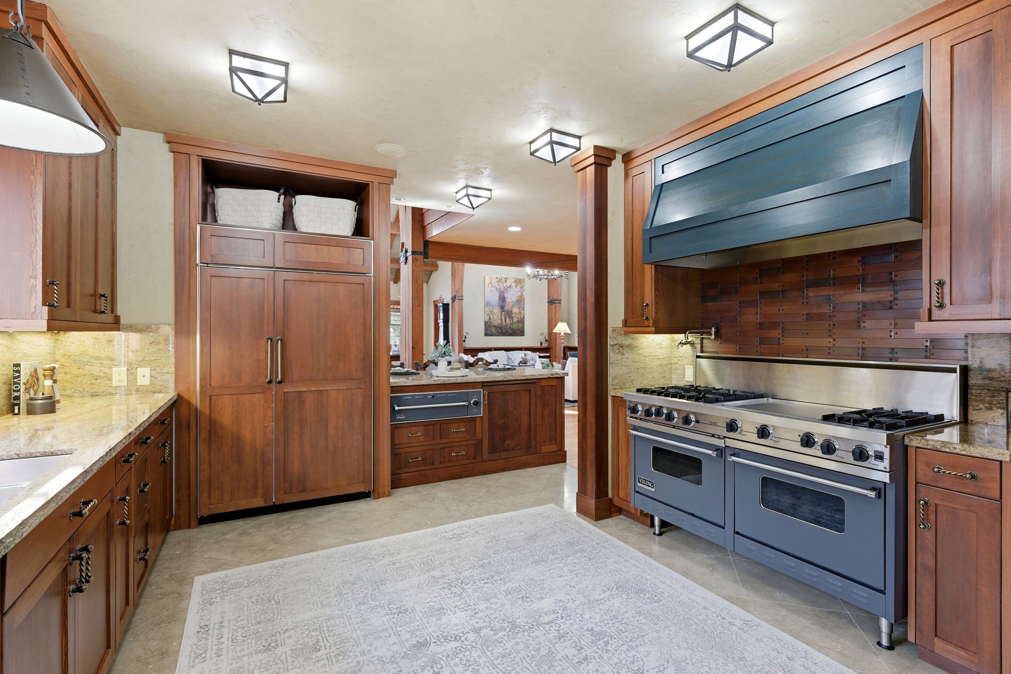 Gourmet kitchen featuring a professional-grade range with double ovens, a custom range hood, wood cabinetry, stone countertops, and an integrated refrigerator