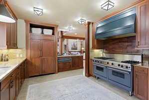Gourmet kitchen featuring a professional-grade range with double ovens, a custom range hood, wood cabinetry, stone countertops, and an integrated refrigerator