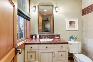 Bathroom featuring a light-toned wood vanity with dark hardware, a red-tiled countertop with an integrated sink, and an ornate framed mirror