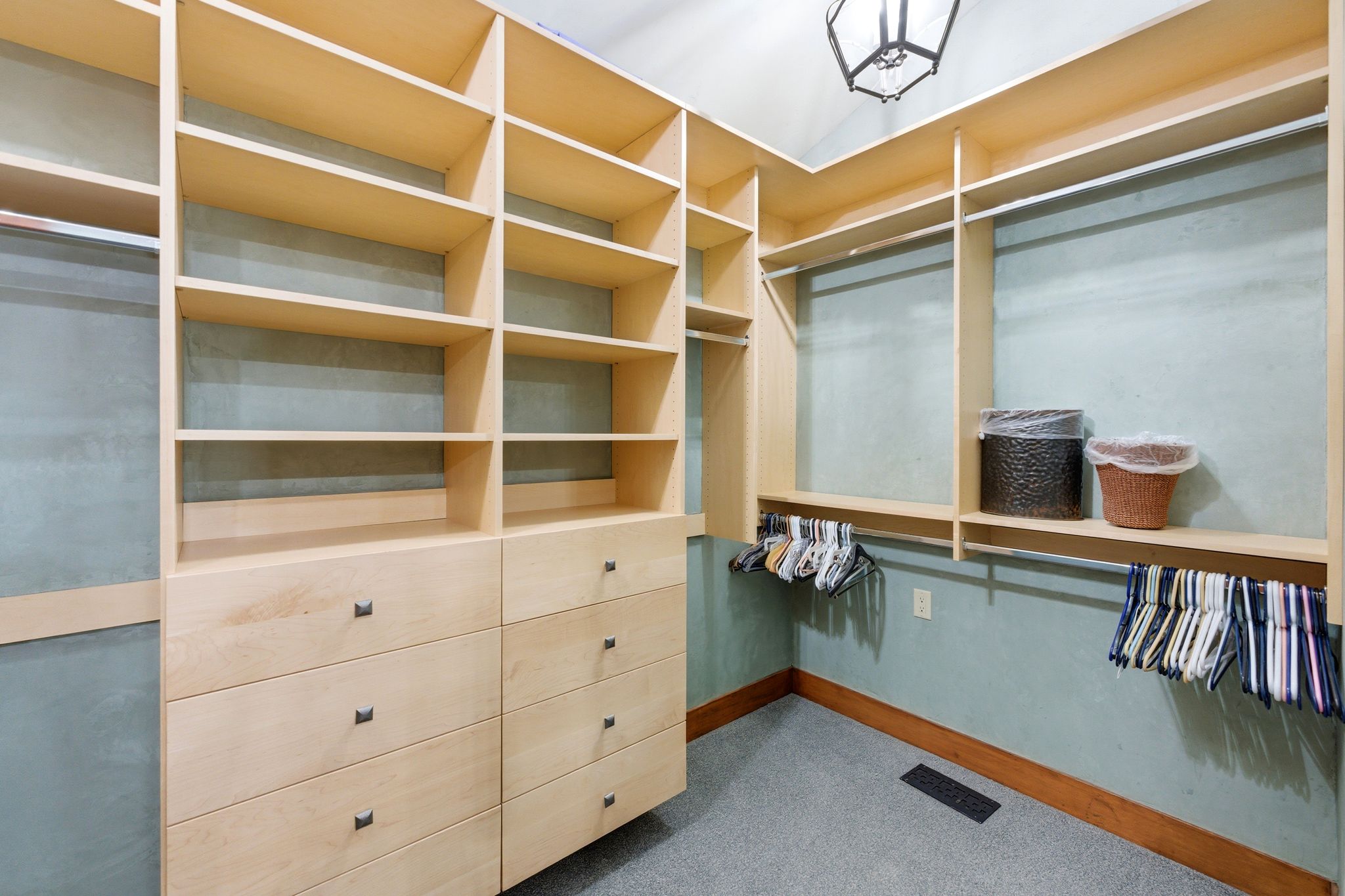 Custom closet system featuring light wood-finish cabinetry, extensive shelving, integrated drawers with dark hardware, and multiple hanging rods