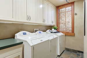 Laundry room featuring extensive upper cabinetry, a built-in countertop, and a window with a natural woven shade