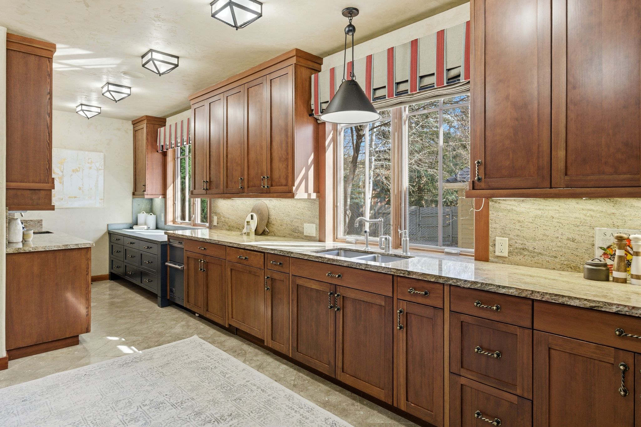Kitchen featuring extensive wood cabinetry, light-toned countertops with a matching backsplash, and a double basin sink under a window