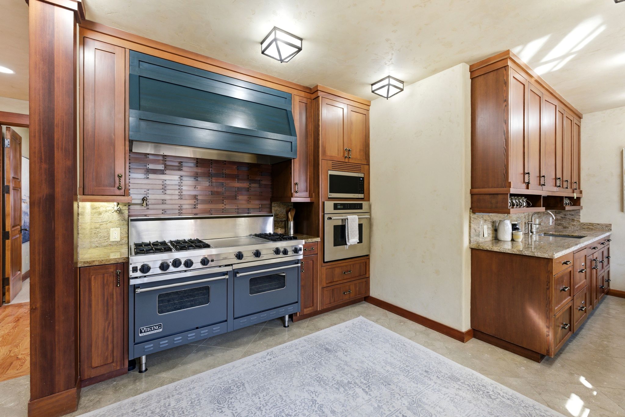 Professional-grade range with a double oven, a custom dark blue range hood, and a brick-patterned backsplash