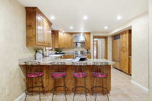 Kitchen featuring a spacious island with a granite-style countertop, abundant wood cabinetry, recessed lighting, stainless steel range hood, and tile flooring