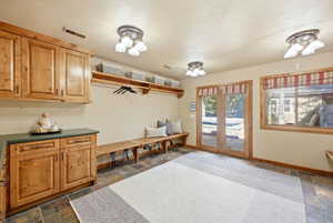Mudroom featuring natural wood cabinetry, slate tile flooring, built-in wooden benches, and French doors