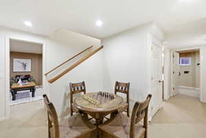Carpeted lower-level recreation area featuring recessed lighting, a wooden staircase with handrails, and a hallway leading to additional rooms