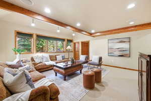 Expansive living area with wood-finish ceiling beams, recessed lighting, and wall-mounted track lighting