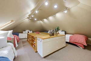 Attic space featuring sloped ceilings, track lighting, light-toned carpeting, and a built-in storage unit with a wood-finish countertop