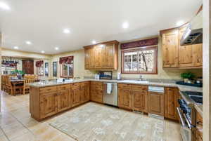 Spacious kitchen featuring extensive wood cabinetry, stone countertops, stainless steel appliances, and tile flooring