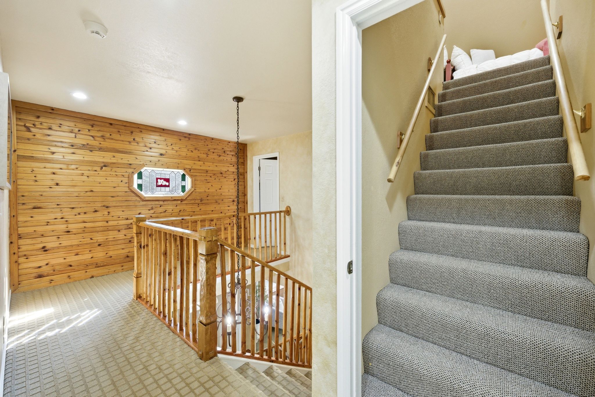 Upper-level landing featuring a wood-paneled accent wall with an octagonal stained-glass window, recessed lighting, and a chandelier