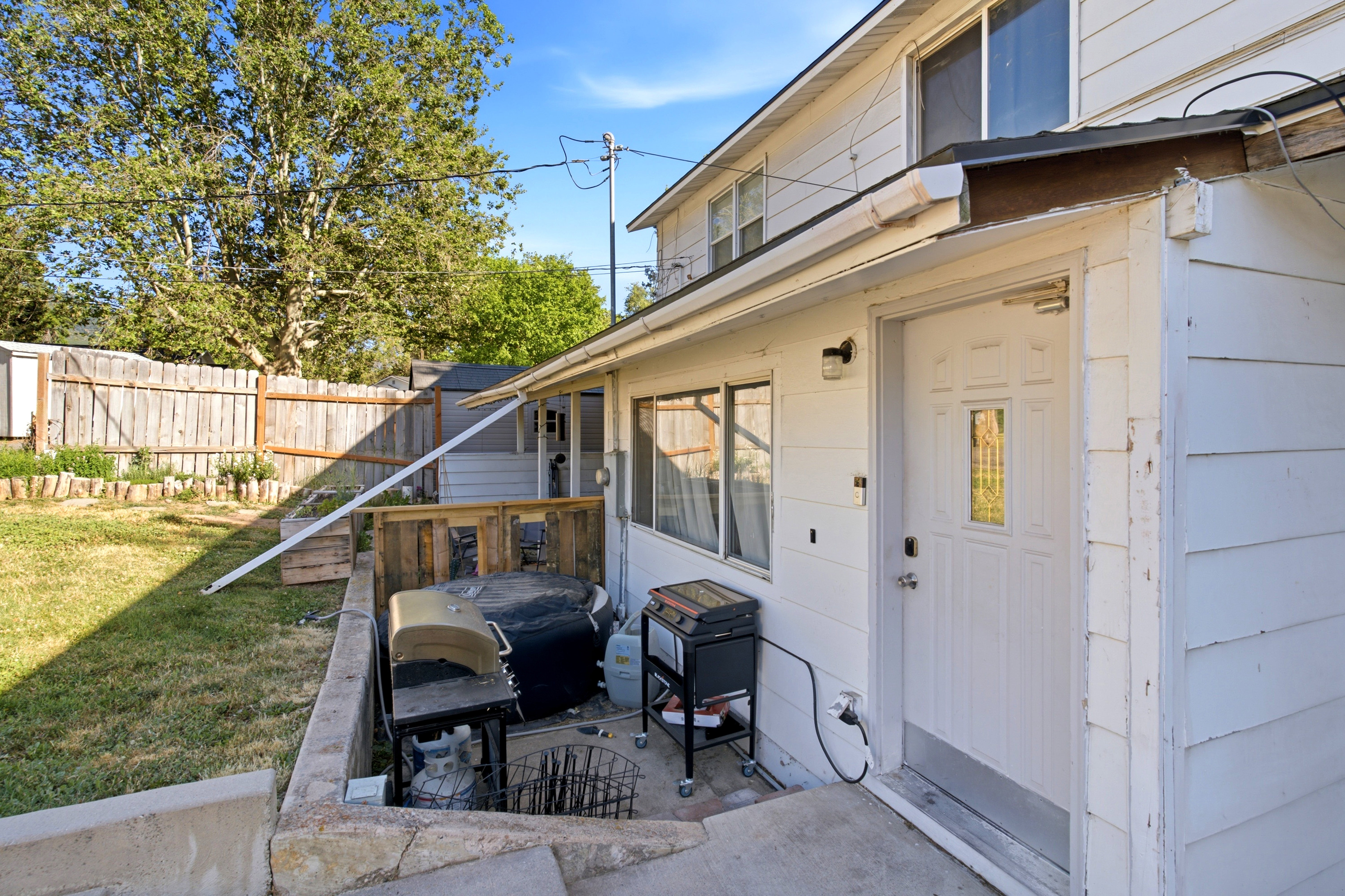 Rear exterior featuring white siding, a multi-pane glass panel door, an outdoor light fixture, and a concrete patio