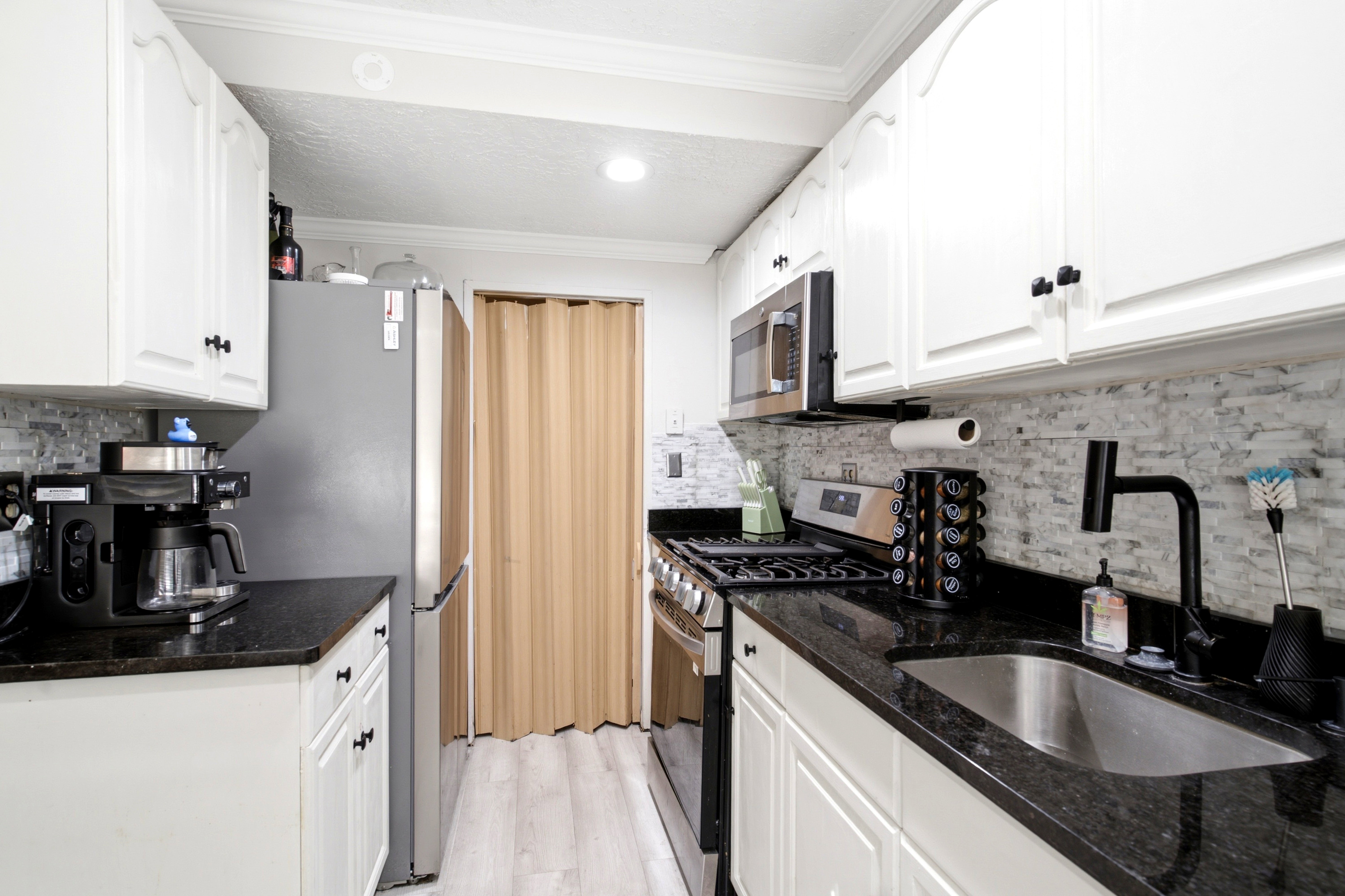 Kitchen featuring white cabinetry with black hardware, dark stone countertops, a stone tile backsplash, stainless steel appliances, and wood-finish flooring