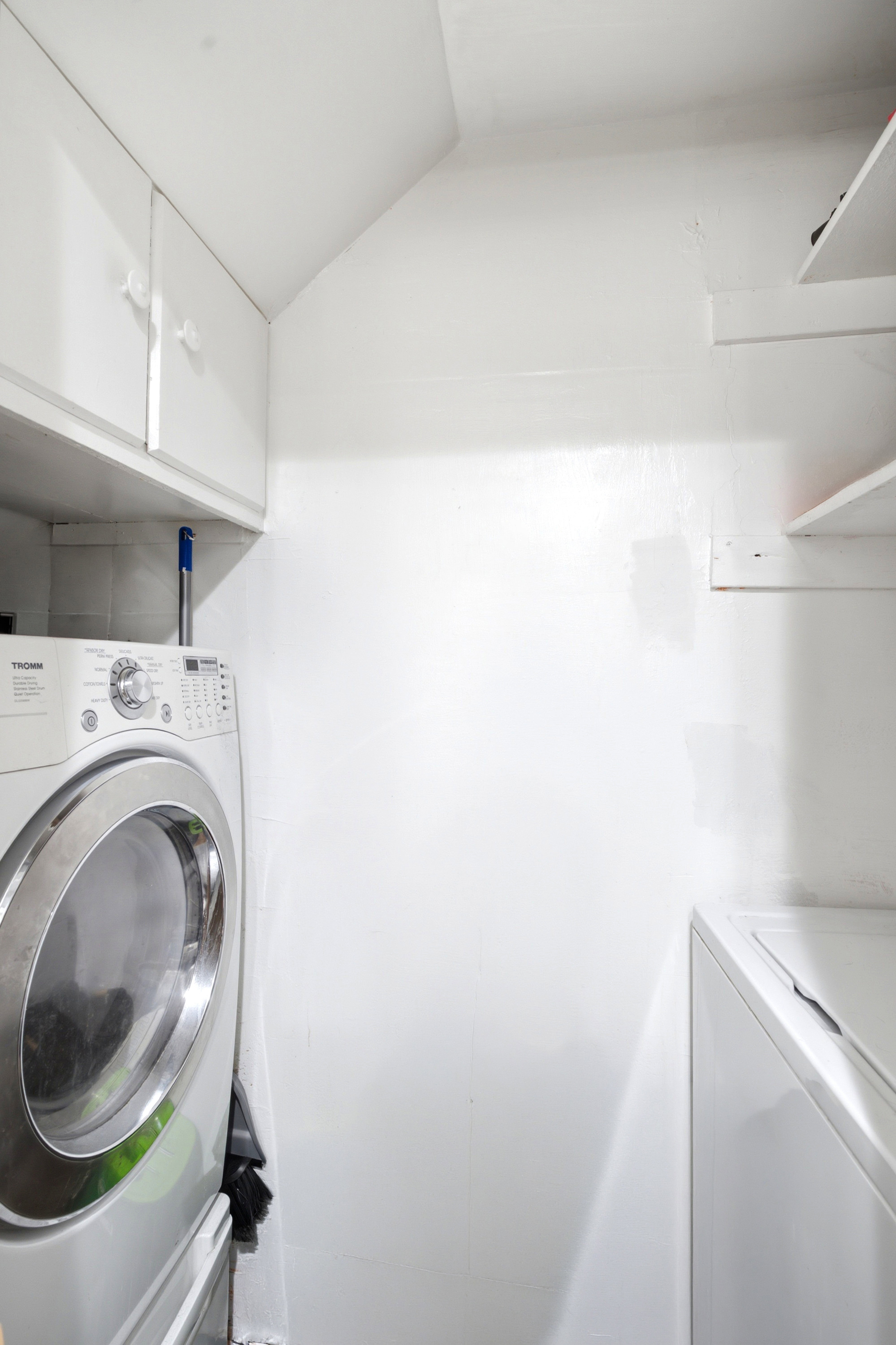 Dedicated laundry area featuring built-in cabinetry, white shelving, and a front-loading washing machine