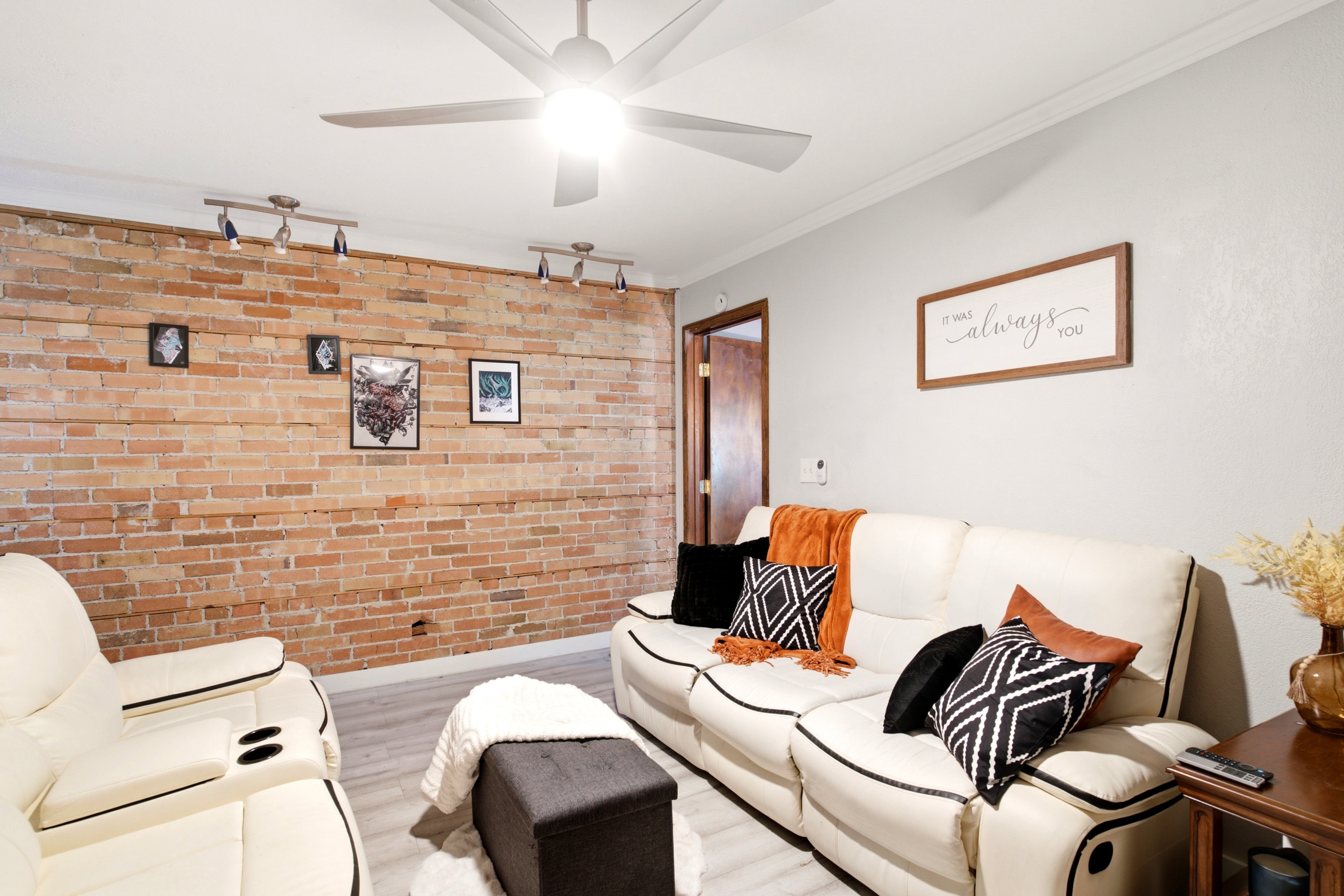 Exposed brick accent wall with track lighting, complementing neutral wall tones and wood-finish flooring