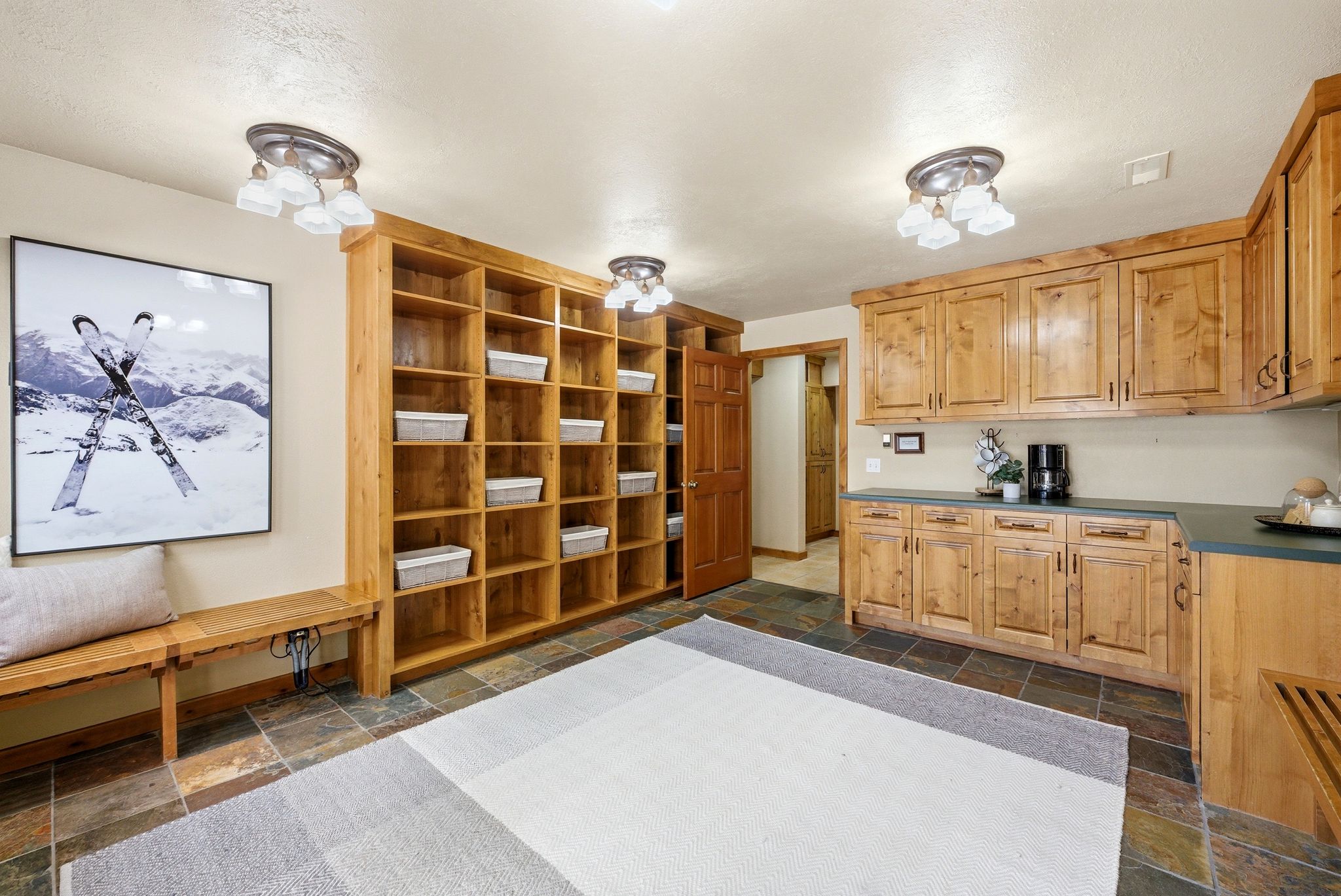 Functional mudroom featuring extensive built-in wooden shelving, coordinating cabinetry with dark countertops, slate tile flooring, and integrated ceiling lights