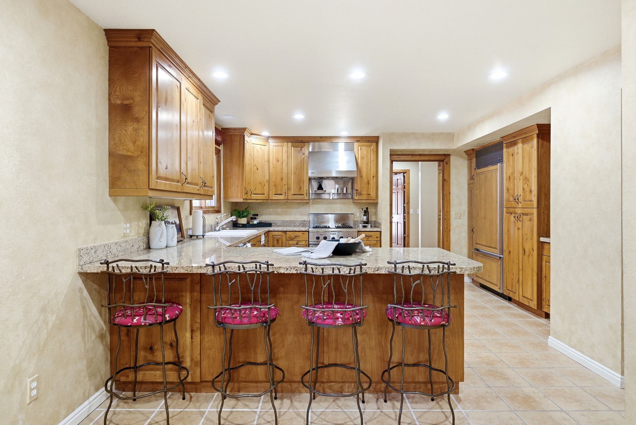 Kitchen featuring natural wood cabinetry, stone countertops, a stainless steel range hood, built-in refrigerator, and recessed lighting