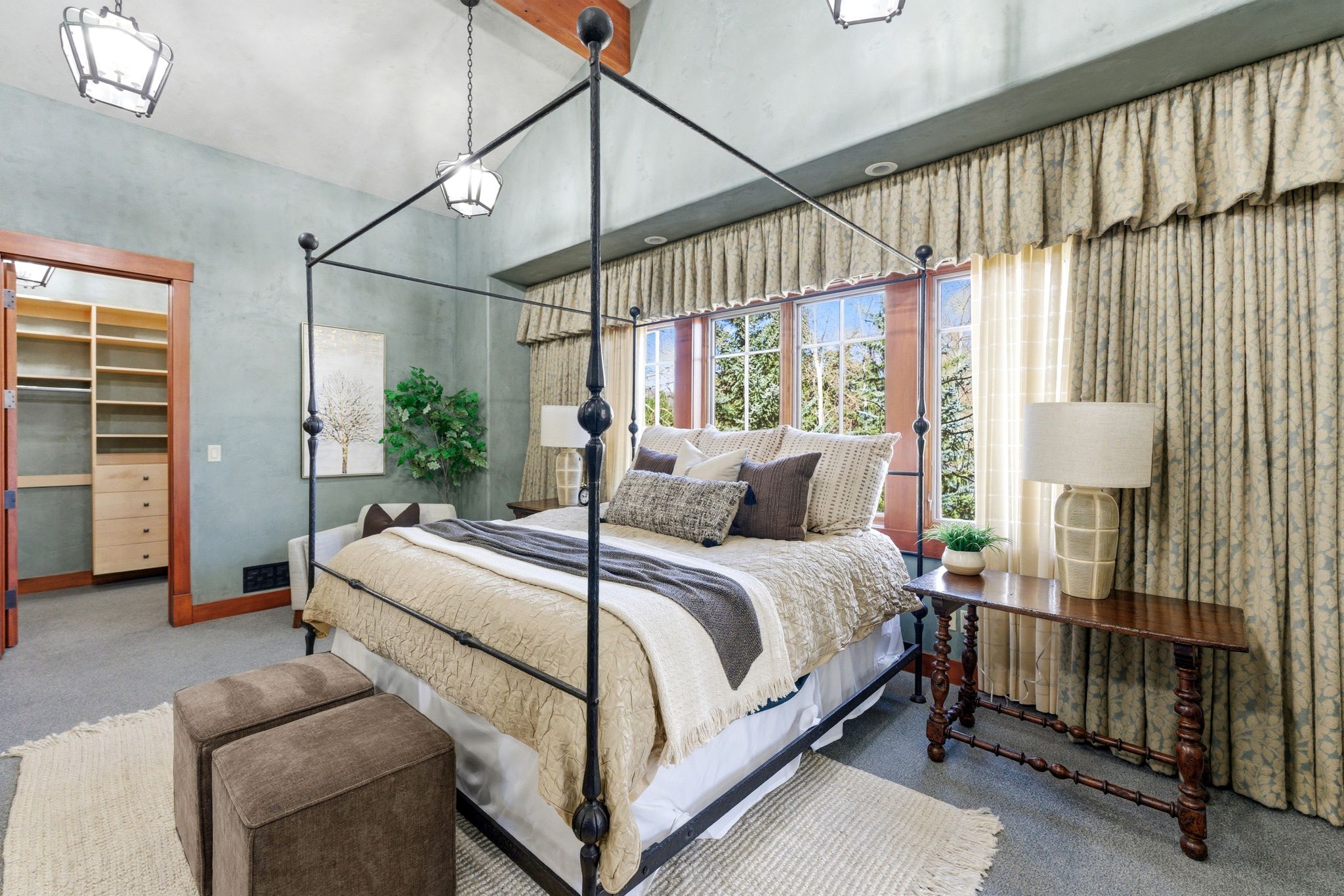Room featuring vaulted ceilings with exposed wood beams, a large window with custom drapery, a built-in closet system with drawers and shelving, and recessed lighting
