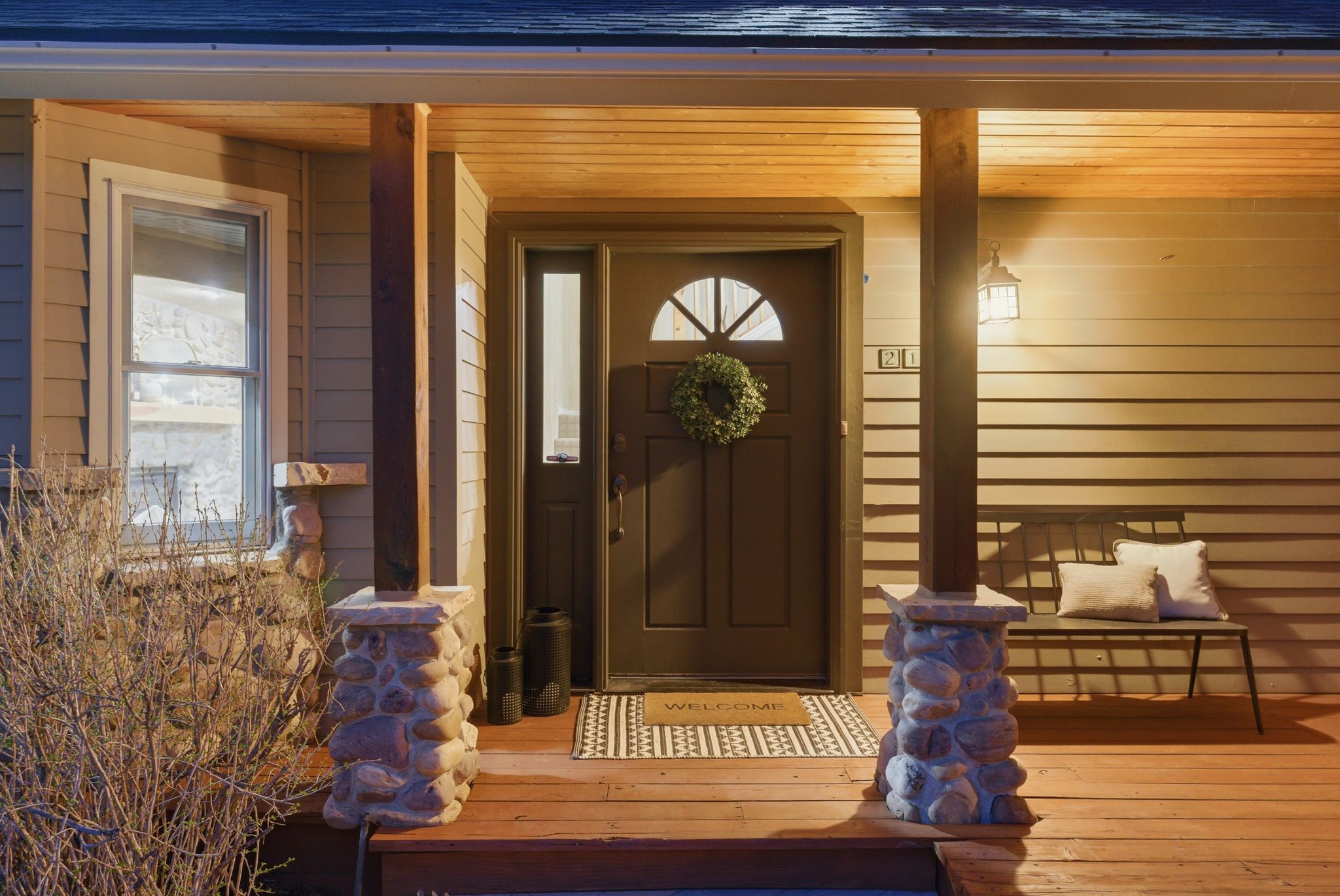 Inviting front porch featuring wood-finish flooring, a solid panel entry door with an arched transom window, and a stone-clad column base