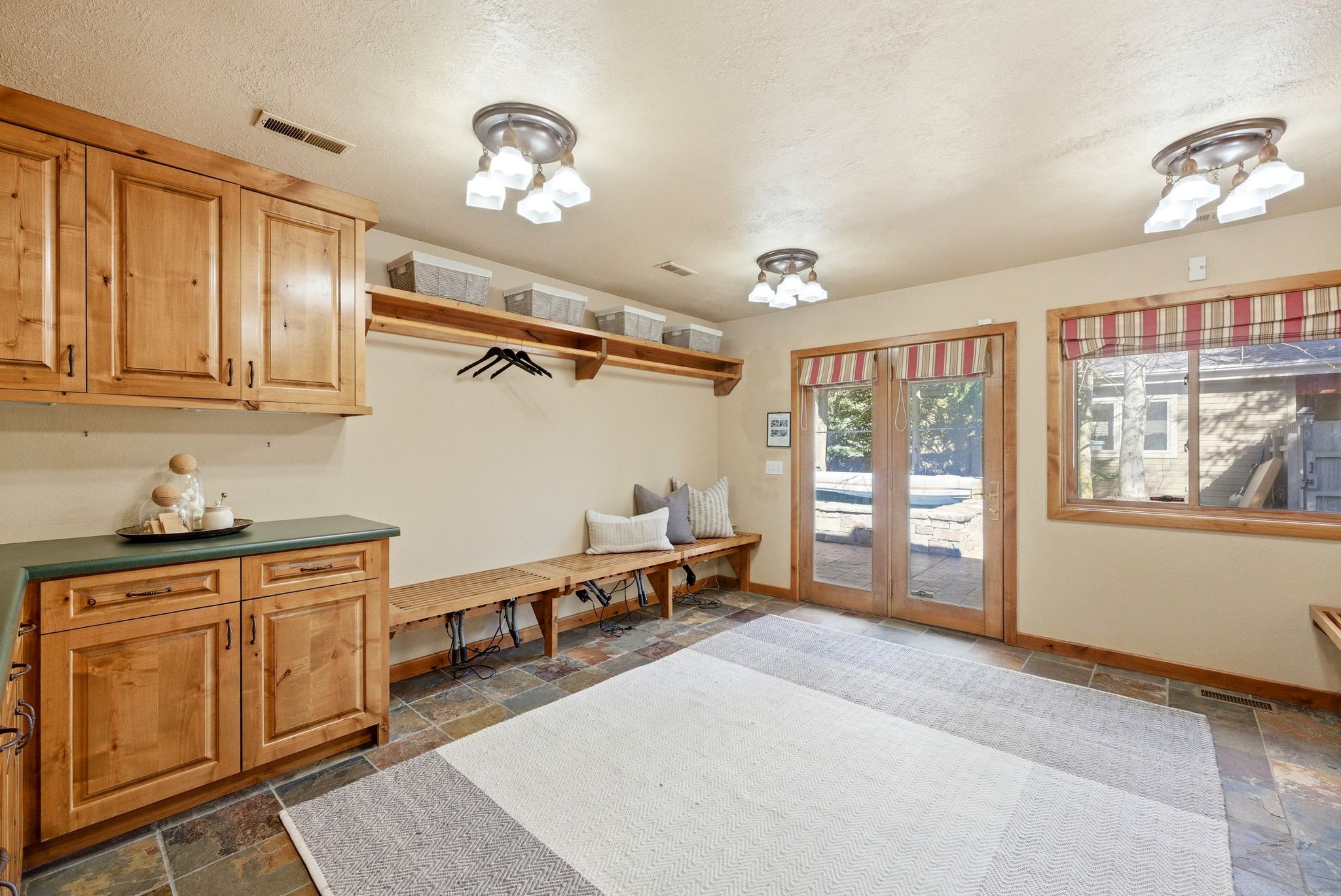 Mudroom featuring natural wood cabinetry, built-in bench seating, slate tile flooring, and double glass-paneled doors