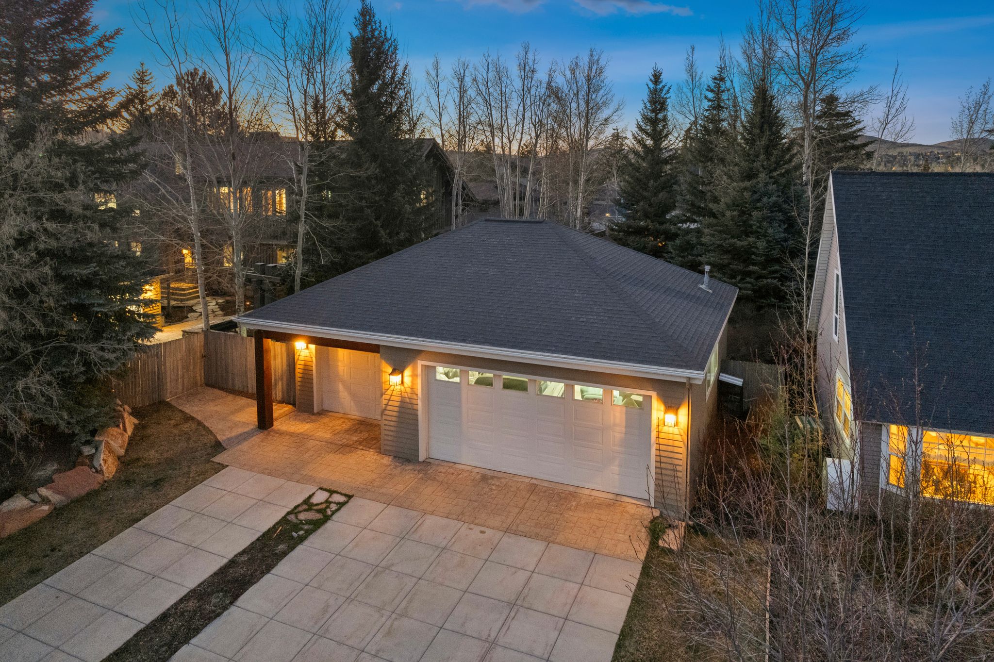 Two-car garage with white paneled doors, exterior lighting fixtures, and a covered entry with a timber support beam