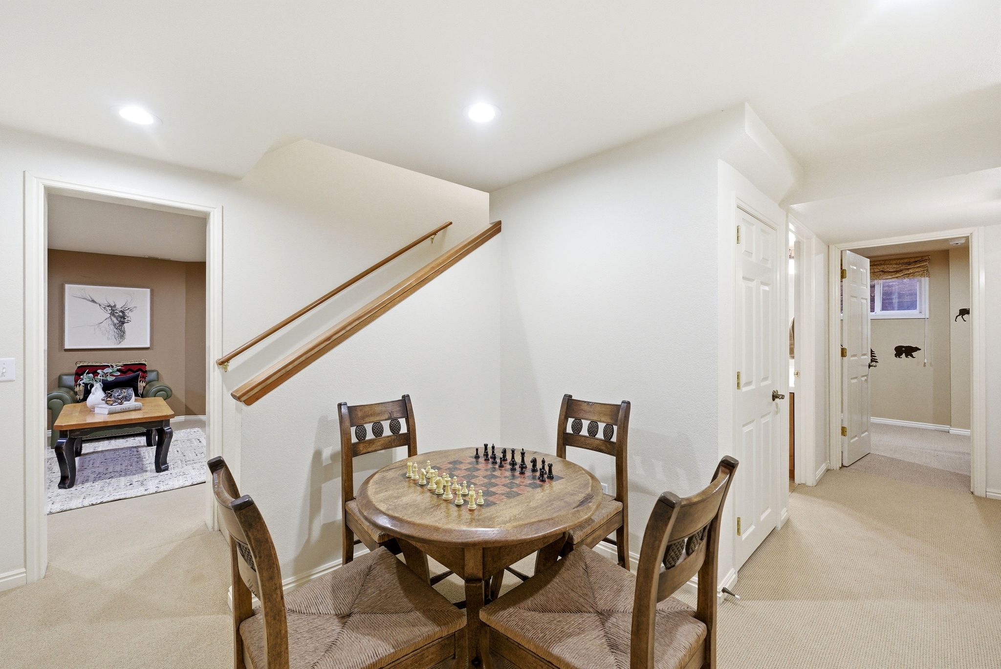Carpeted recreation room featuring a wooden game table, solid wood handrails, recessed ceiling lights, and multiple doorways providing access to additional spaces