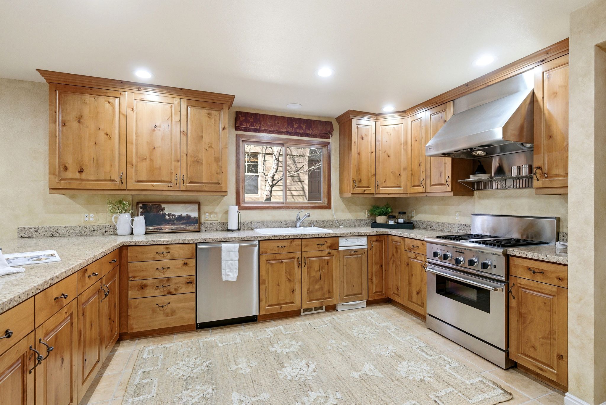 Kitchen featuring abundant wood cabinetry, light-toned countertops, a stainless steel range with a matching range hood, and a built-in dishwasher