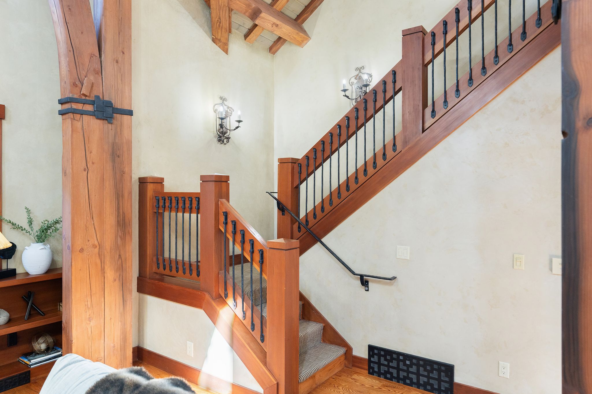 Crafted timber staircase featuring wrought iron balusters and sconce lighting