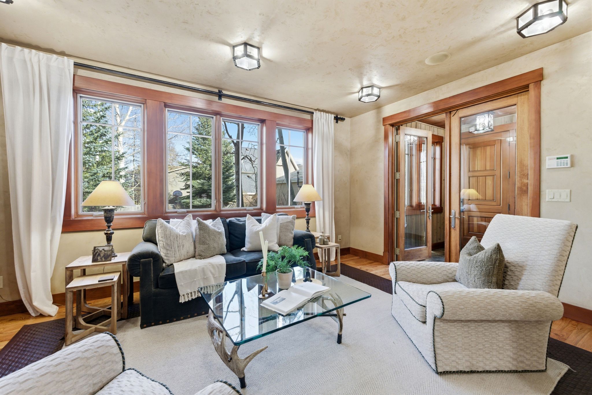 Living area featuring a wall of multi-pane windows with wood trim, hardwood flooring, and a pair of glass-paned French doors with wood framing