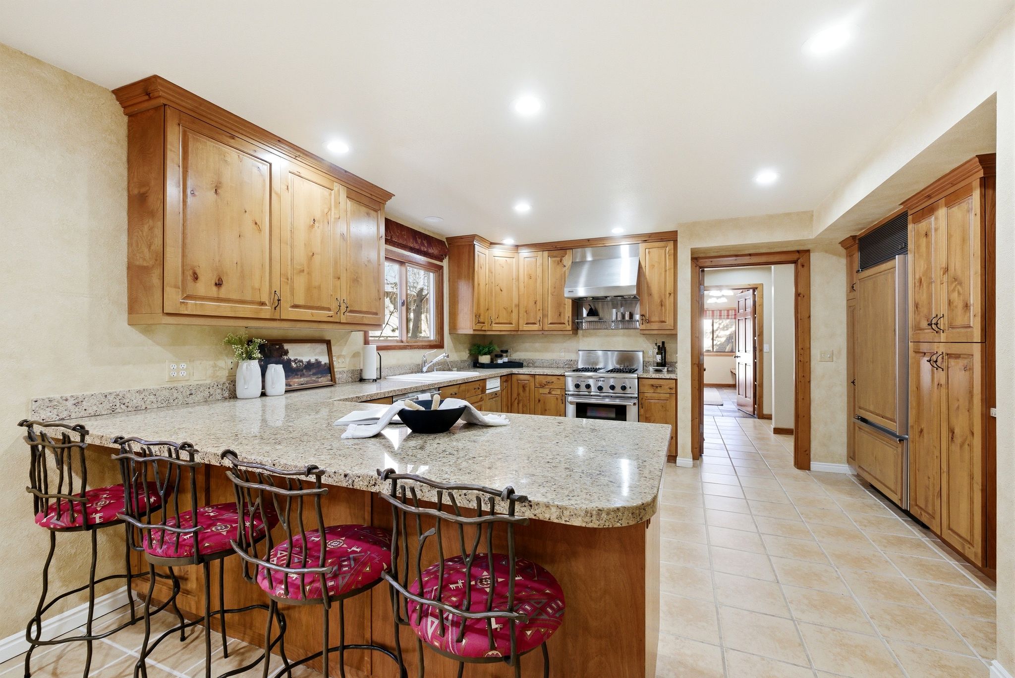 Spacious kitchen featuring light wood cabinetry, recessed lighting, a large island with a stone-finish countertop, stainless steel appliances, and tile flooring