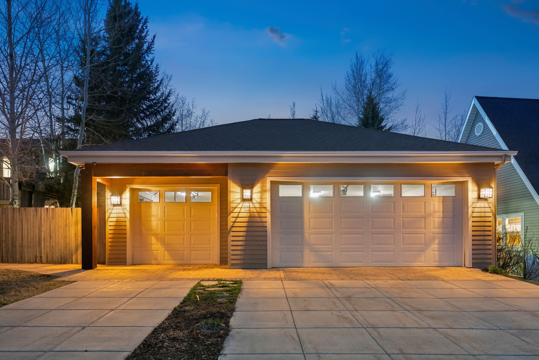 Two-car garage with overhead lighting and a single-car garage featuring exterior sconces and a wood beam accent