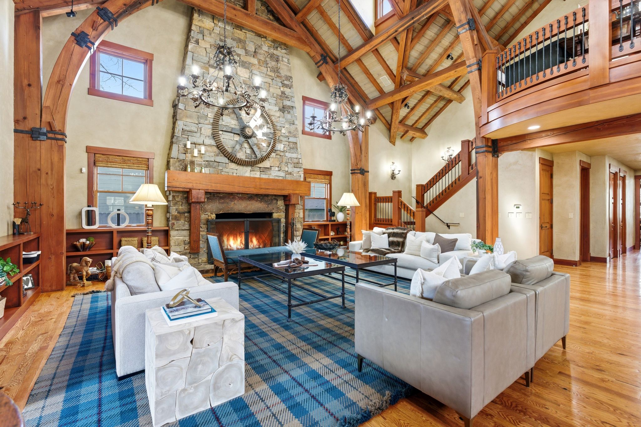 Spacious living area featuring a vaulted wood-beam ceiling, stone-clad fireplace with a wood mantle, wood-finish flooring, and a built-in staircase
