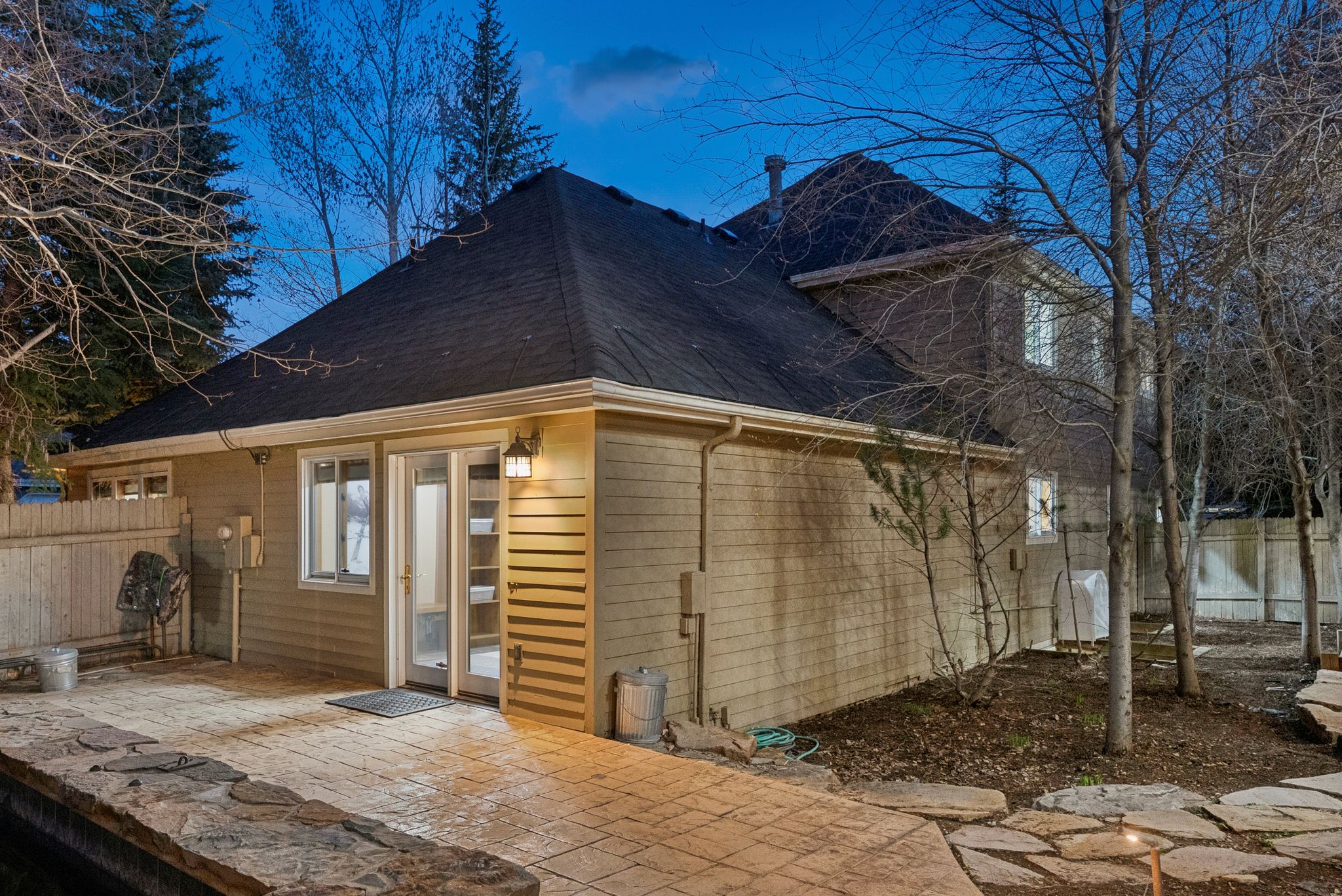 Rear exterior featuring a stamped concrete patio, stone retaining wall, and mature trees