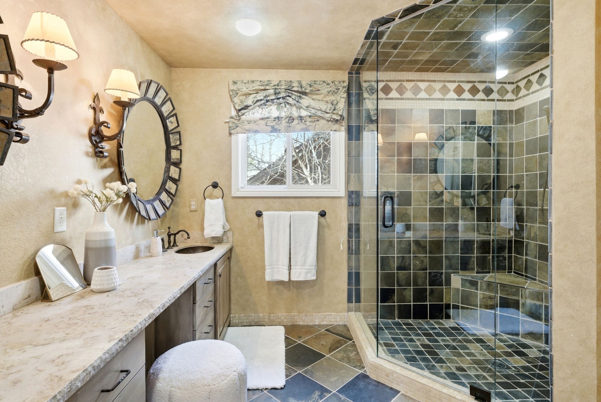 Walk-in shower with tiled walls and floor, vanity with stone countertop, built-in cabinetry, and wall-mounted sconces