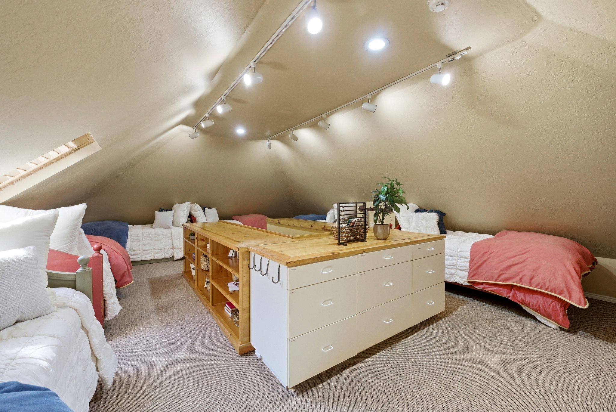 Carpeted attic space featuring a sloped ceiling, track lighting, and a built-in storage island with drawers and shelving