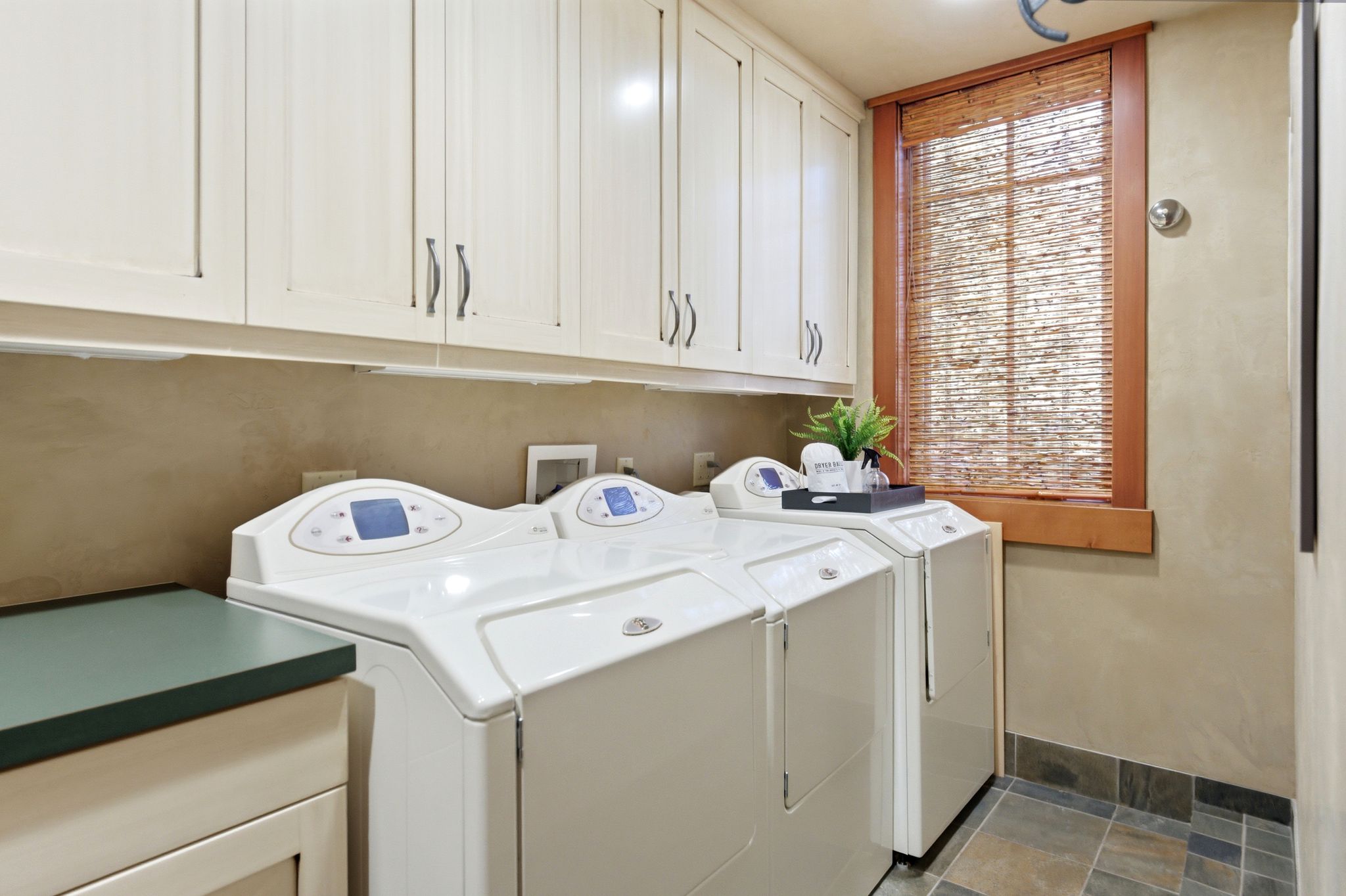 Laundry room featuring extensive upper cabinetry, a built-in countertop, and a window with a natural woven shade