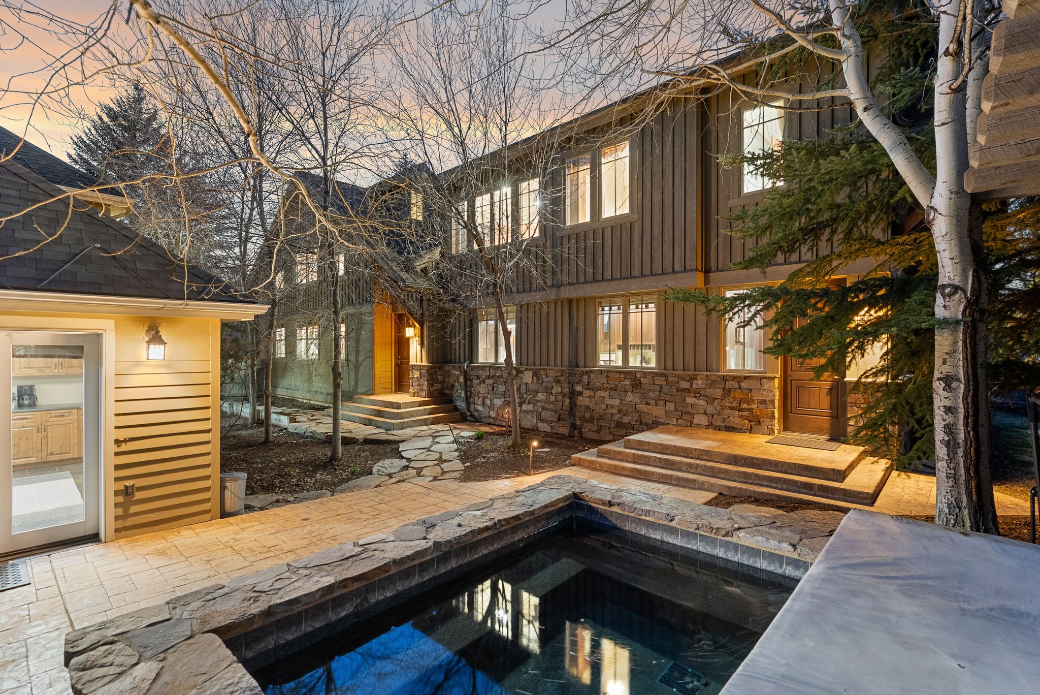 Exterior features a stone-surround spa with stone coping, a paved patio, and a separate structure with horizontal wood siding