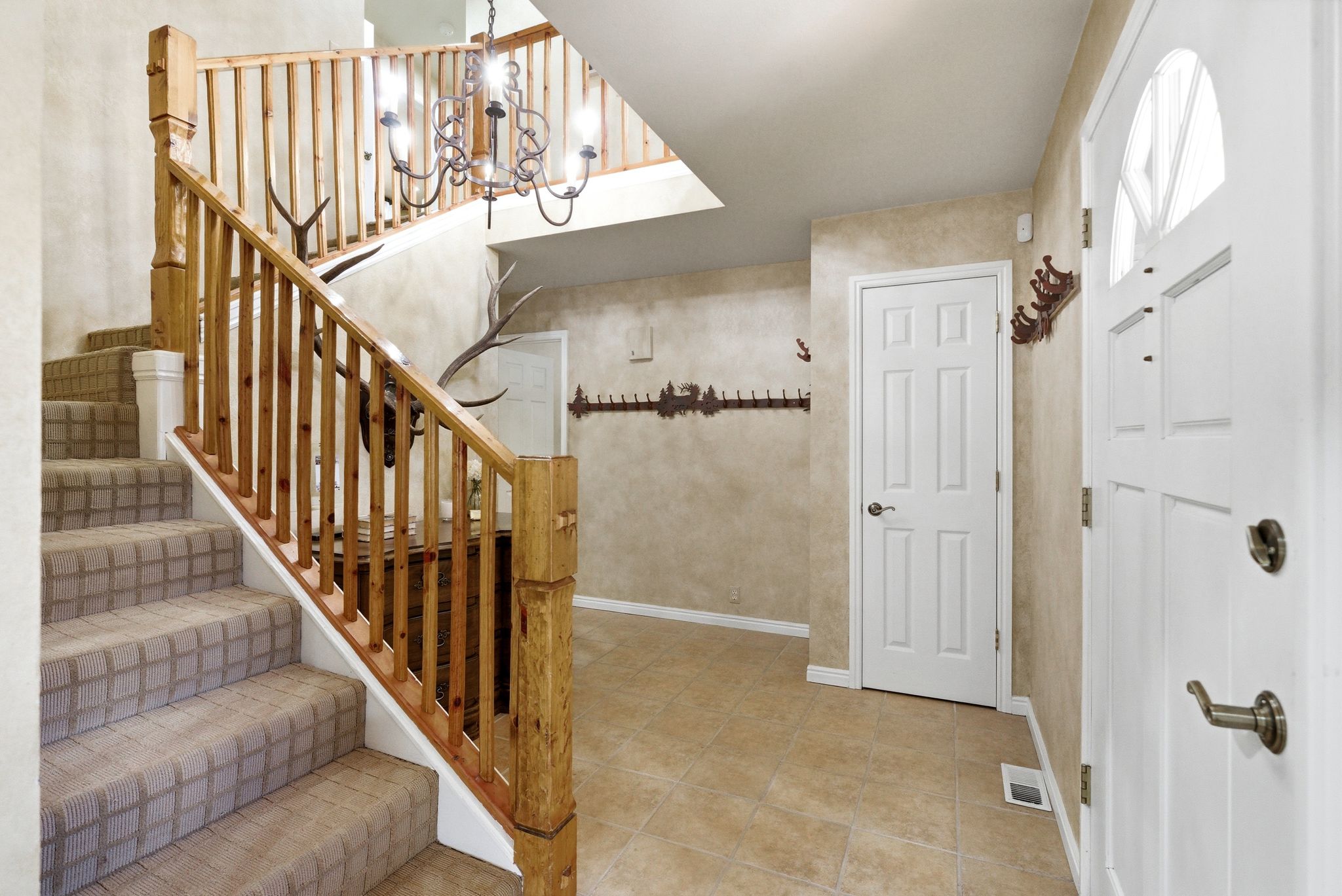 Entry foyer featuring a carpeted staircase with wood banister, tile flooring, and a white paneled entry door with an arched window