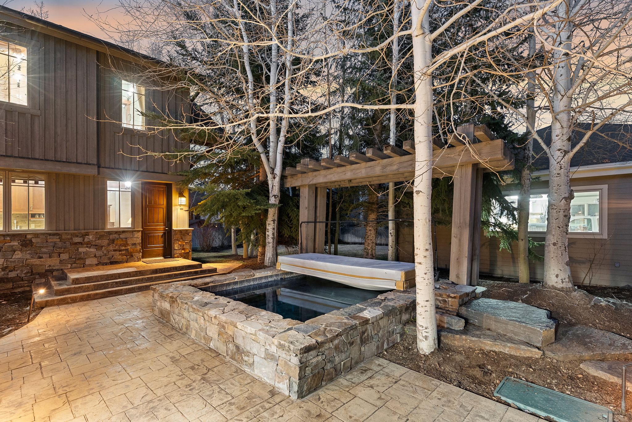 Exterior patio featuring a stone-clad hot tub with an overhead wooden pergola