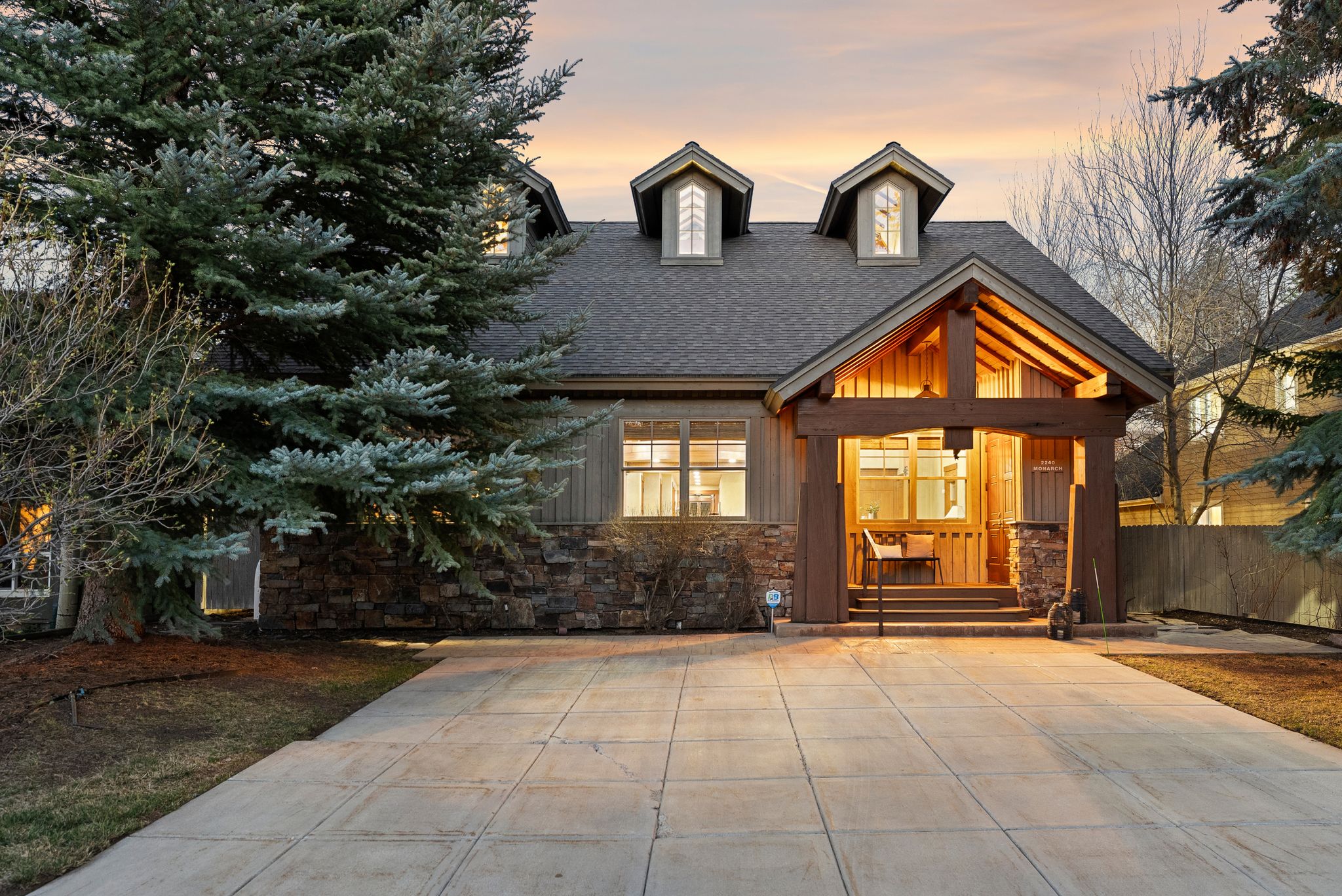 Craftsman-style exterior with a deep covered porch, exposed wood beams, dormer windows, and a stone facade