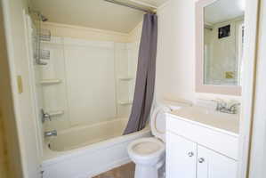 Bathroom featuring a white bathtub with a shower, a white single-sink vanity with a laminate countertop, and a framed mirror