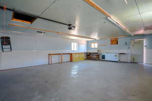 Spacious garage with concrete flooring, multiple windows, built-in shelving, workbenches, and ceiling-mounted lighting fixtures